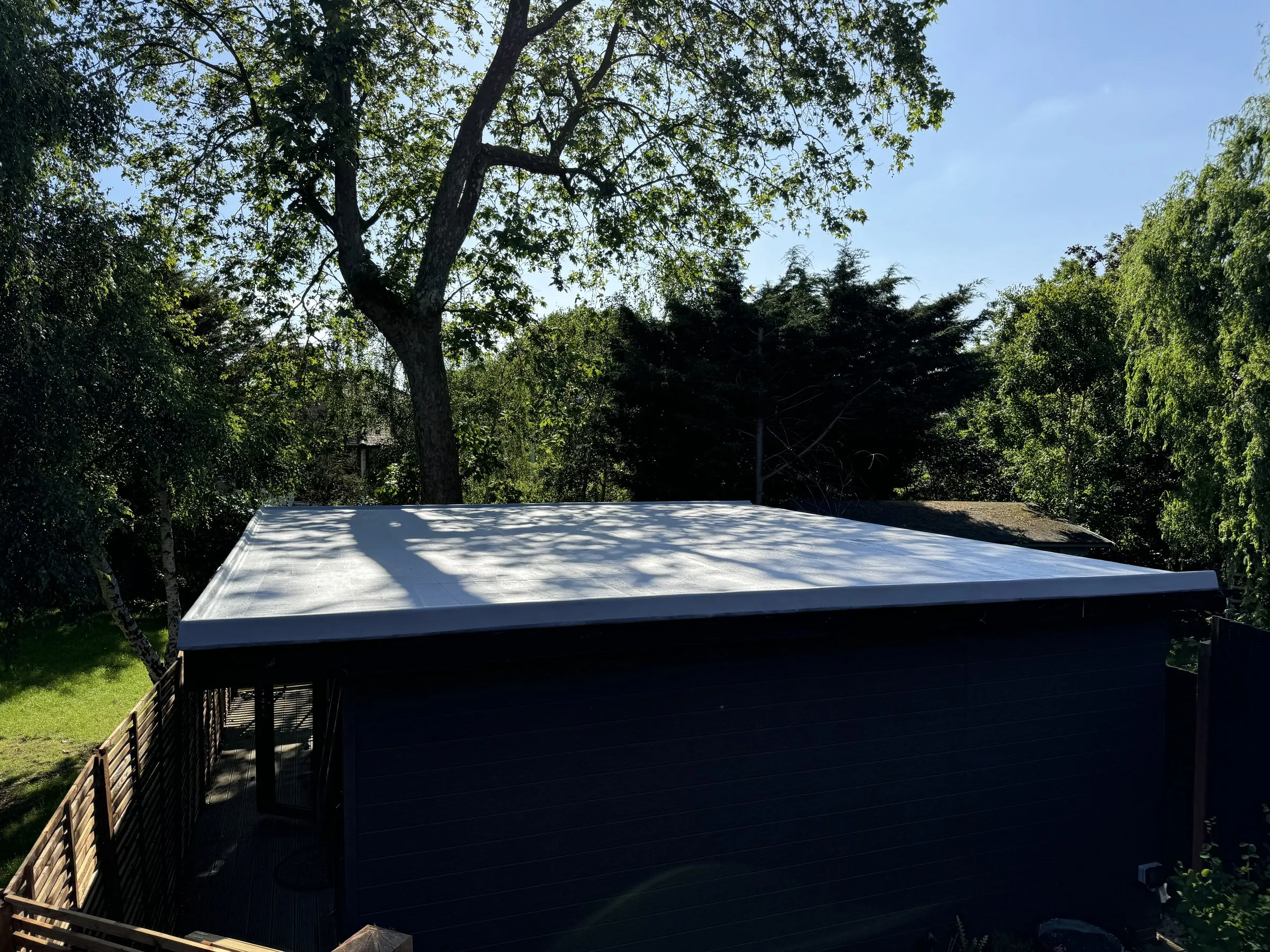 A graphite flat roof sealed with the HYDRONYLON liquid-applied waterproofing system, on an outbuilding in a garden