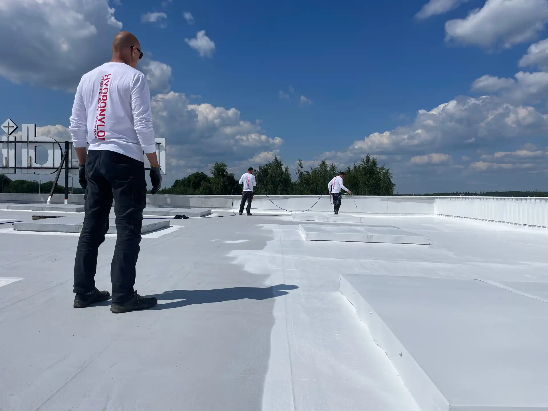 Contractors applying the HYDRONYLON liquid system on a large flat roof